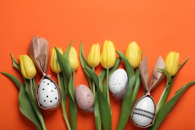 Photo of Easter bunnies made of craft paper and eggs among beautiful tulips on orange background, flat lay