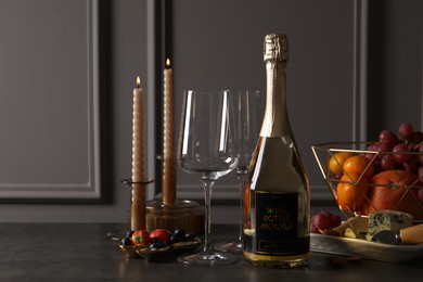 Photo of Bottle of sparkling wine, glasses, candles and delicious snacks on grey table