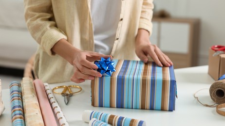 Woman wrapping gift at white table indoors, closeup