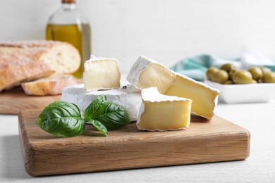 Tasty brie cheese with basil on white wooden table