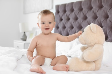 Adorable little baby with teddy bear on bed at home