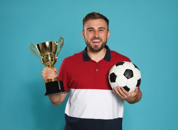 Portrait of happy young soccer player with gold trophy cup and ball on blue background