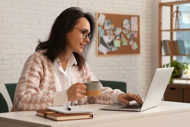 Woman with modern laptop and cup of tea learning at home