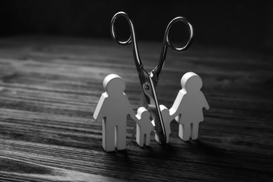 Family figure and scissors on black wooden table. Relationship problems concept