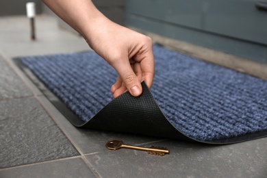 Photo of Woman's hand lifting door mat to reveal key hidden underneath, closeup