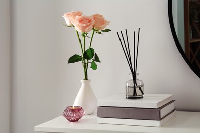 Photo of Roses, candle and reed diffuser on white console table in room