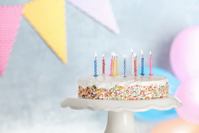 Tasty birthday cake with burning candles on stand against blurred background, space for text