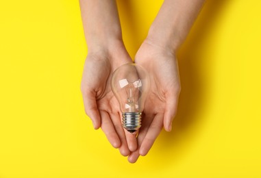 Woman holding light bulb on yellow background, top view