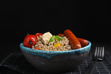 Tasty buckwheat porridge with sausages on table against black background