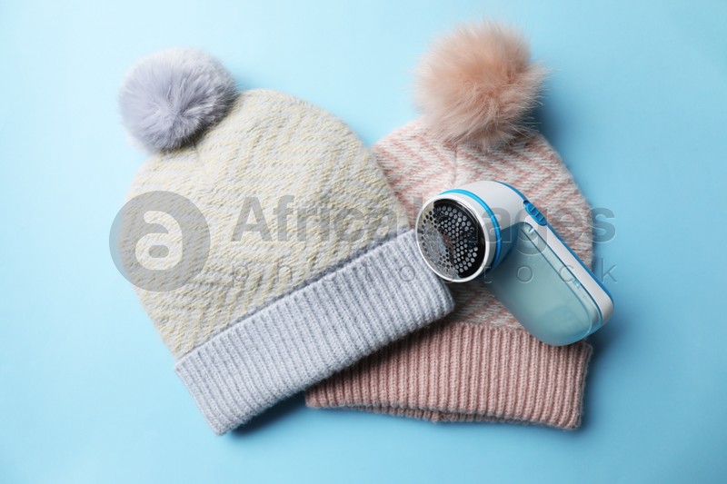Photo of Modern fabric shaver and woolen hats on light blue background, flat lay