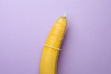Banana with condom on lilac background, top view. Safe sex concept