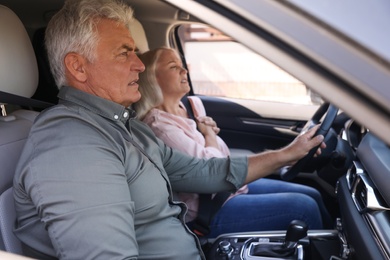 Image of Senior man holding steering wheel while his wife having heart attack in car