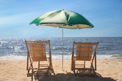 Green beach umbrella and deck chairs on sandy seashore