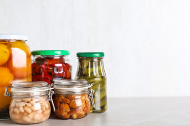 Glass jars with different pickled vegetables on light marble table. Space for text