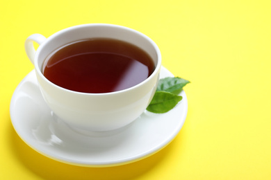 Cup of aromatic black tea and green leaves on yellow background