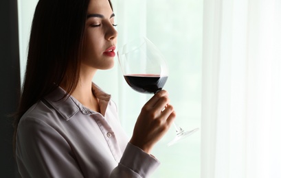 Beautiful young woman with glass of luxury red wine indoors. Space for text