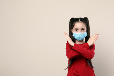 Little girl in medical mask on beige background, space for text. Virus protection