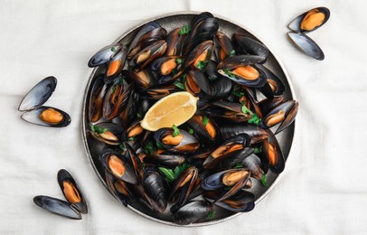 Plate with cooked mussels, parsley and lemon on white tablecloth, flat lay