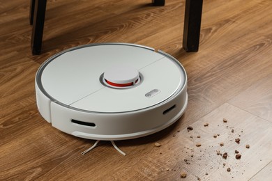 Photo of Robotic vacuum cleaner removing dirt from wooden floor indoors