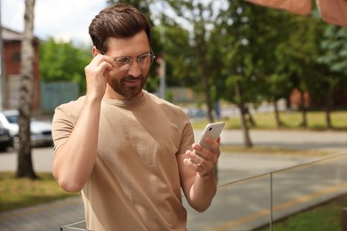 Smiling handsome bearded man with smartphone outdoors. Space for text