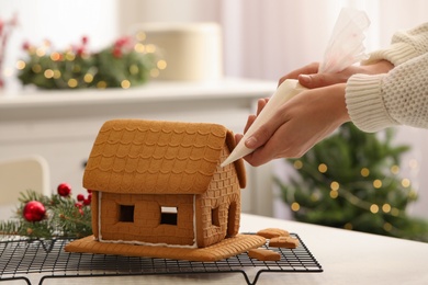 Woman making gingerbread house at white table, closeup