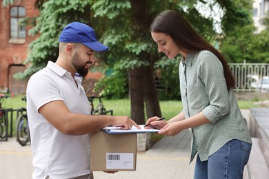 Woman signing for delivered parcel outdoors. Courier service
