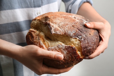 Woman breaking freshly baked bread on grey background, closeup
