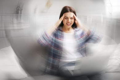 Young woman with laptop suffering from migraine at home