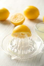 Plastic juicer with half of lemon on white wooden table