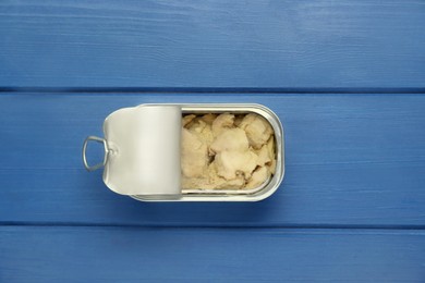 Photo of Open tin can of tasty cod liver on blue wooden table, top view