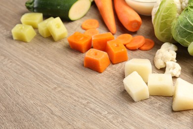 Photo of Different frozen purees cubes and fresh vegetables on wooden table. Space for text
