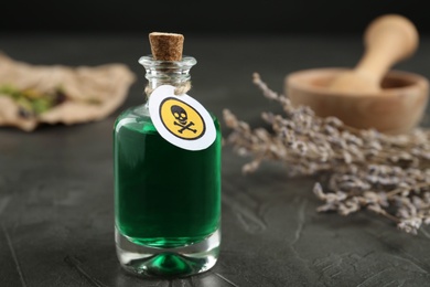 Glass bottle of poison with warning sign and herb on grey stone table