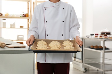 Female pastry chef holding baking sheet with uncooked croissants in kitchen, closeup
