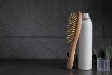 Dry shampoo spray, eucalyptus branch and hairbrush on dark table near grey wall. Space for text