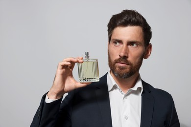 Photo of Handsome bearded man with bottle of perfume on light grey background. Space for text