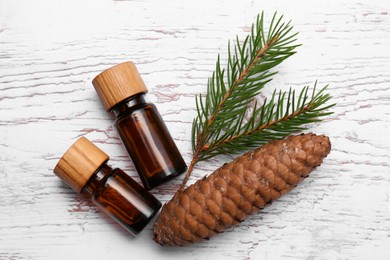 Bottles of pine essential oil, conifer tree branch and cone on white wooden table, flat lay
