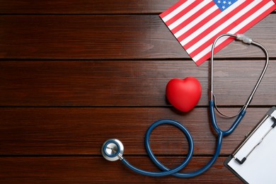 Stethoscope, red heart, clipboard and American flag on wooden table, flat lay. Space for text