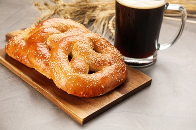 Tasty pretzels, glass of beer and wheat spikes on grey table
