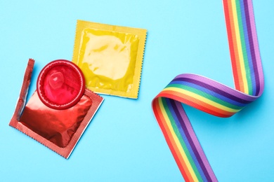 Colorful condoms and rainbow ribbon on light blue background, flat lay. LGBT concept