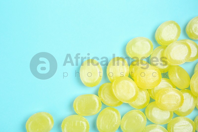 Many delicious lemon drops on light blue background, flat lay. Space for text