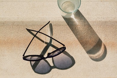 Stylish sunglasses and glass of water on stone surface outdoors, flat lay