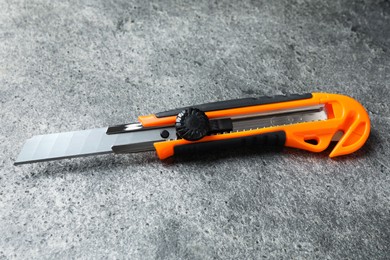 Photo of Orange utility knife on grey table. Construction tool