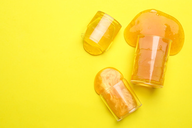 Photo of Overturned plastic containers with bright slimes on yellow background, top view. Space for text