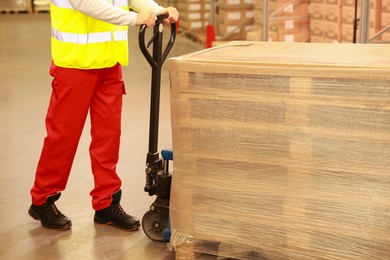 Worker moving wrapped wooden pallets with manual forklift in warehouse, closeup