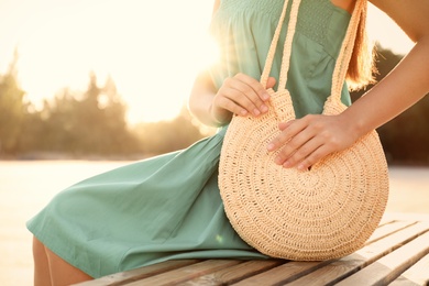Young woman with stylish straw bag on bench outdoors, closeup