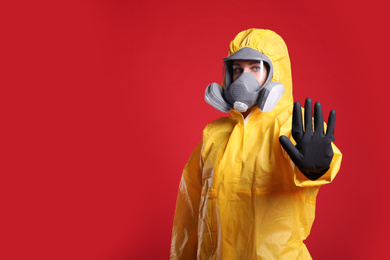 Woman in chemical protective suit making stop gesture on red background, space for text. Virus research