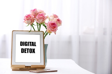 Tablet with phrase DIGITAL DETOX, smartphone and flowers indoors. Space for text