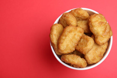 Bucket with delicious chicken nuggets on red background, top view. Space for text