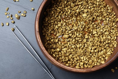 Bowl of gold nuggets and tweezers on black table, flat lay