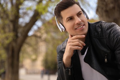 Handsome man with headphones listening to music outdoors, space for text